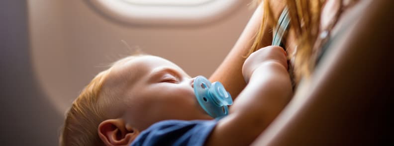 Sleeping toddler with pacifier during flight showing in flight sleep strategy A toddler with a pacifier sleeps in a caregiver’s arms during a daytime flight, highlighting sleep and nap time solutions when flying with toddlers