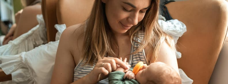 Staying Grounded While Traveling With a Baby Calm Moments Matter Mother gently holding and smiling at her baby while relaxing in bed during a quiet moment traveling with a baby