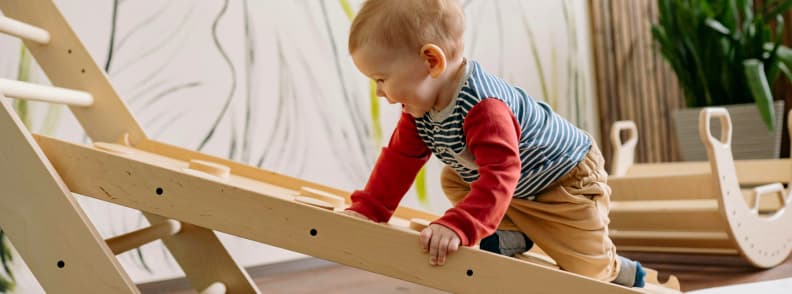 Toddler climbing in indoor play area representing airport amenities and play zones for children Happy toddler climbing on wooden play equipment in a clean, indoor setting, illustrating the value of airport amenities and play areas for families flying with toddlers