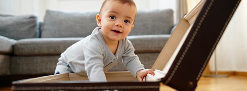Toddler packing suitcase representing packing and carry on essentials for flying with young children Smiling toddler packing an open suitcase at home, capturing the importance of packing and carry-on essentials when flying with toddlers