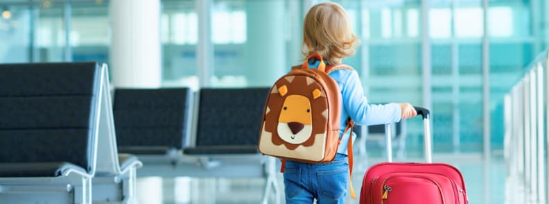 Toddler with lion backpack and red suitcase walking through airport terminal – flying with toddlers tips for air travel, carry-on luggage, and airport travel with kids