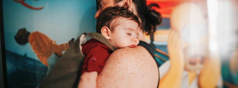toddler jet lag recovery tips Parent holding a sleeping toddler in a busy terminal, showing the importance of rest and real-life toddler jet lag recovery tips after a long flight