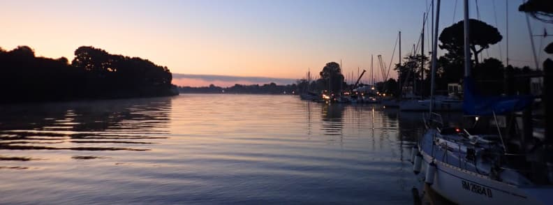 Arno River sunrise sunset photography spots Sunrise over the Arno River at Nautica 180 Pisa, with soft reflections and sailboats docked quietly, illustrating one of the most peaceful Arno River sunrise sunset photography spots during a sailing Tuscany trip.