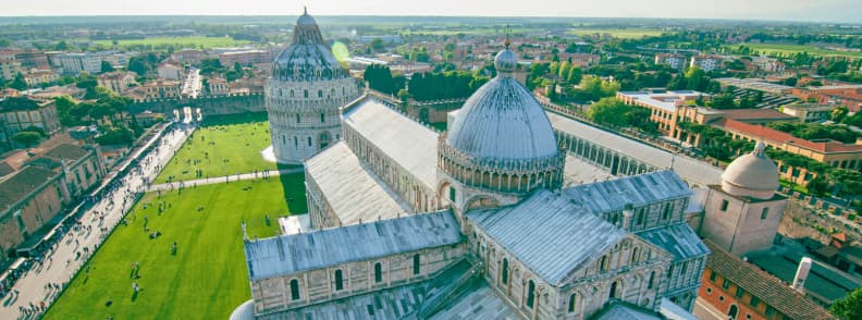 Visit Pisa travel guide: Aerial view of Pisa Cathedral, Pisa Baptistery, and Leaning Tower of Pisa with green lawns and surrounding cityscape