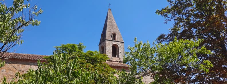 Abbaye du Thoronet Bell Tower Why Visit in Provence Bell tower of Abbaye du Thoronet rising above lush trees under a clear summer sky in Provence, France