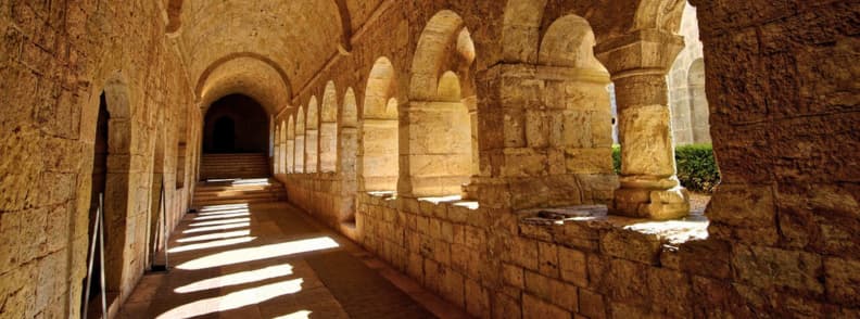 Cloister Corridor of Le Thoronet Monastery Cistercian Abbey Provence Stone corridor of the cloister at Abbaye du Thoronet in Provence with Romanesque arches and doorways leading to the dormitory, refectory, and armarium