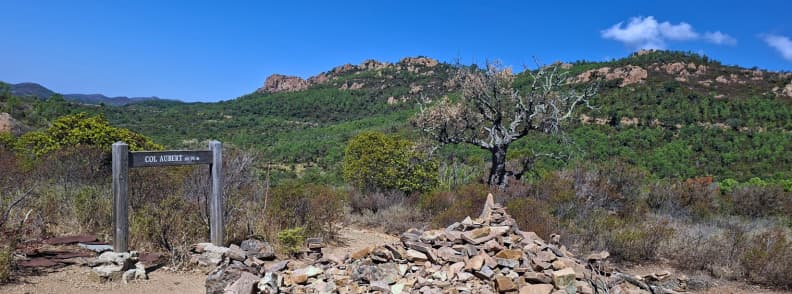Col Aubert pass trail forks Esterel Massif Saint Raphael Signpost and cairn marking the Col d’Aubert trail junction in the Estérel Massif with red rock hills and pine forest near Saint-Raphaël