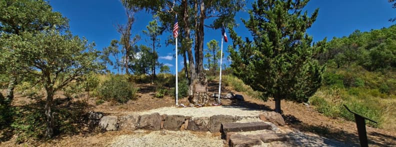Col de Belle Barbe World War II memorial Esterel Massif Saint Raphael Memorial with flags and plaque beneath a tall eucalyptus at Col de Belle Barbe in the Estérel Massif Saint Raphael honoring the Lucky Lady B 24 Liberator crew on the Chemin de Mémoire