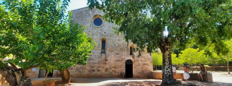 Entrance to Abbaye du Thoronet Church Guided and Self Guided Tours Provence Main entrance of Abbaye du Thoronet in Provence with visitors resting under shaded trees