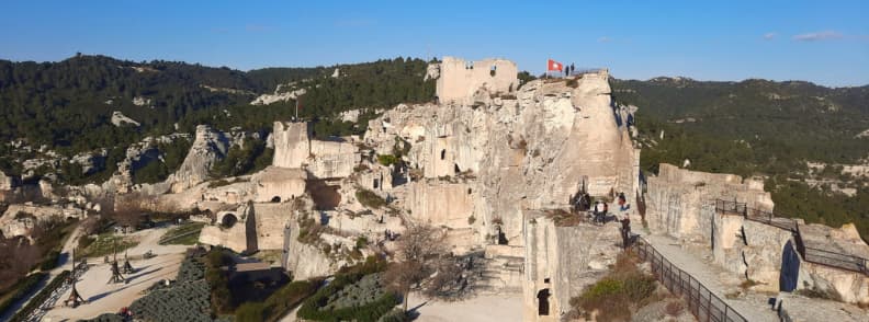 Panoramic view of the Château des Baux-de-Provence with fortress ruins, towers, and siege engines set against the Alpilles hills