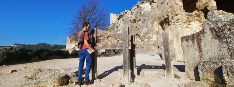 Visitor standing next to a reconstructed medieval pillory at the Château des Baux-de-Provence, part of the historic fortress ruins in southern France