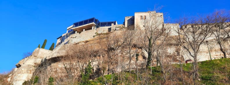 Stone buildings and restaurant terrace above the cliffs behind the Musée des Santons in Les Baux-de-Provence under a clear blue sky