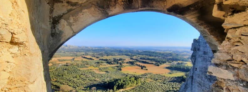 Landscape view through an arched window of the Château des Baux-de-Provence overlooking olive groves and the Alpilles countryside