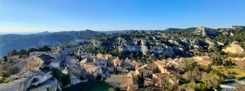 Panoramic view of Les Baux-de-Provence with stone houses, medieval fortress ruins, and the surrounding Alpilles hills under a clear blue sky