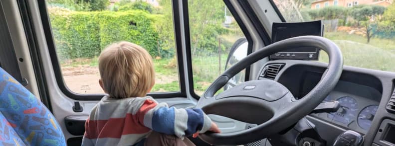 Camper Van Family Travel Cotignac Provence Toddler sitting in the driver’s seat of a camper van in Cotignac France, looking out the windshield before a family road trip.