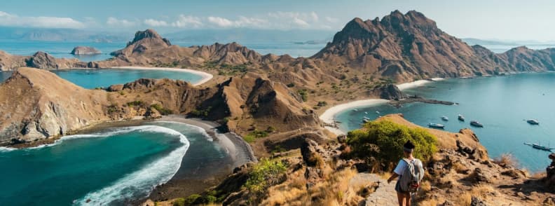 Traveler standing on a trail overlooking Padar Island’s bays and rugged hills in Komodo National Park, Indonesia.
