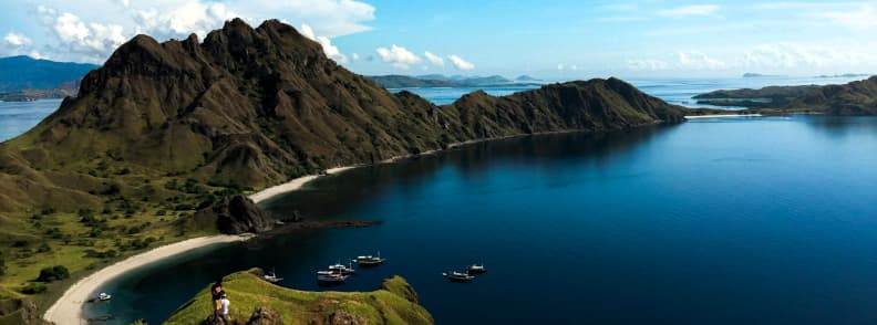 View of Padar Island in Komodo National Park, Indonesia, with turquoise waters, green hills, and anchored boats.