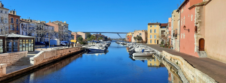 Martigues canal Etang de Berre itinerary Provence travel Canal lined with colorful houses and boats in Martigues, leading toward the modern bridge and blue sky, part of an Étang de Berre travel itinerary.