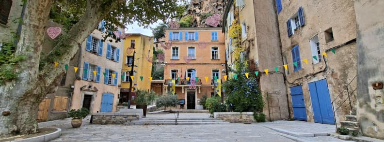 Place de la Mairie Cotignac Village Square Provence Colorful houses on Place de la Mairie in Cotignac France decorated with flags and hearts under the cliffside tuff rock known as Le Rocher.