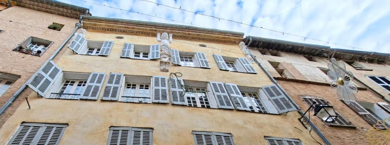Things to see in Cotignac Cariatides Facade Historic Architecture Provence Facade of an old stone house on Grande Rue in Cotignac France with restored 17th-century Cariatides and pastel shutters under a blue Provençal sky.