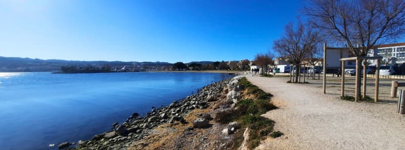 parking Etang de Berre Martigues walking path Jardins de la Rode Path along the Étang de Berre near Jardins de la Rode in Martigues, with calm blue water, trees, and a clear walking trail leading toward the town center.