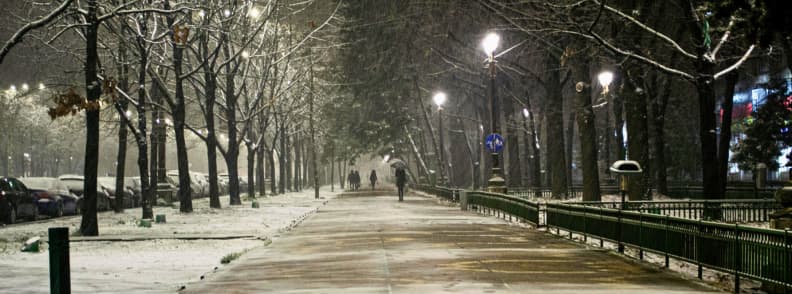 Snowy evening walkway in Bucharest with streetlights and people walking through a quiet winter scene.