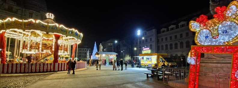 Nearly empty Bucharest Downtown Christmas Market before 6 pm with carousel lights and festive decorations.