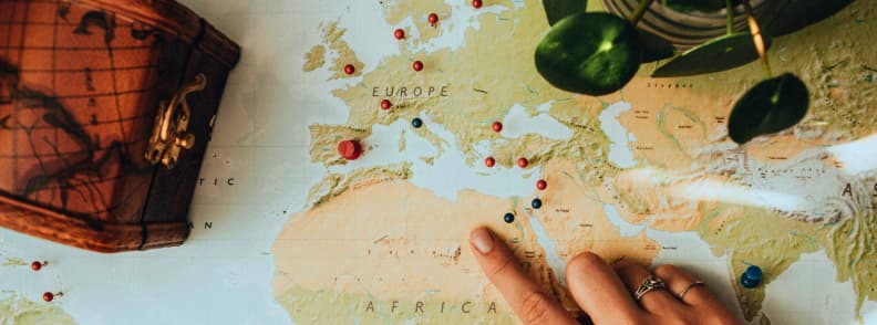 International travel insurance full route coverage Hand pointing at a world map with travel pins marking multiple international destinations