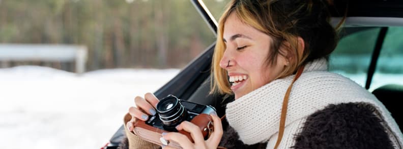 Traveler holding a camera inside a car during a winter road trip in Europe