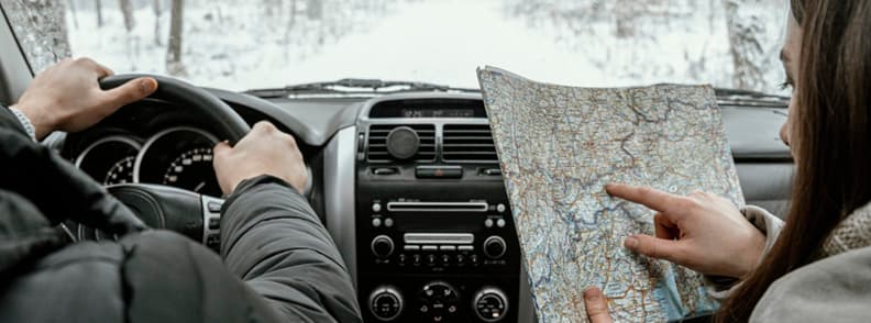 Travelers inside a car reading a paper map during a winter road trip in Europe
