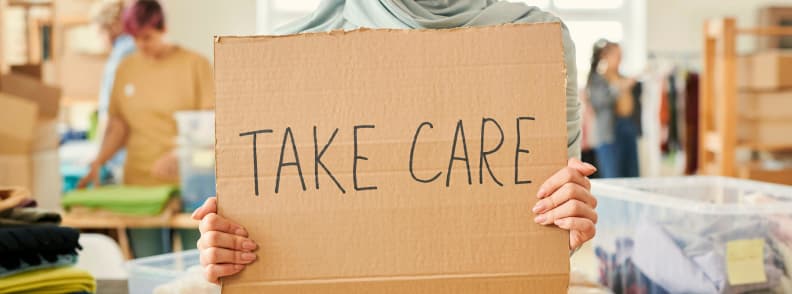 holiday donation ideas. person holding a cardboard sign reading take care inside a community donation and support center