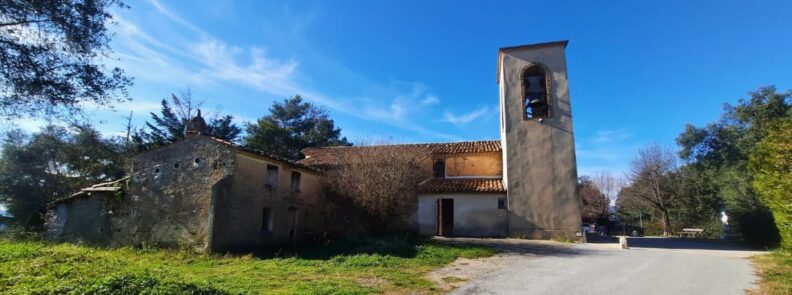 Notre Dame de Peygros church and bell tower on a hilltop in Tanneron surrounded by trees under a clear blue sky