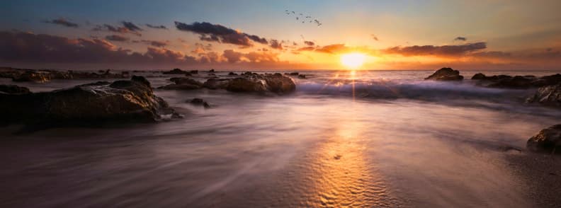 Sunset over the ocean at Boucan Canot beach on the west coast of Réunion Island with waves washing over rocks