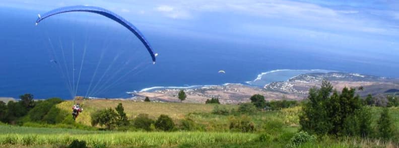 Paraglider taking off above Saint-Leu on Réunion Island with the west coast and lagoon visible below