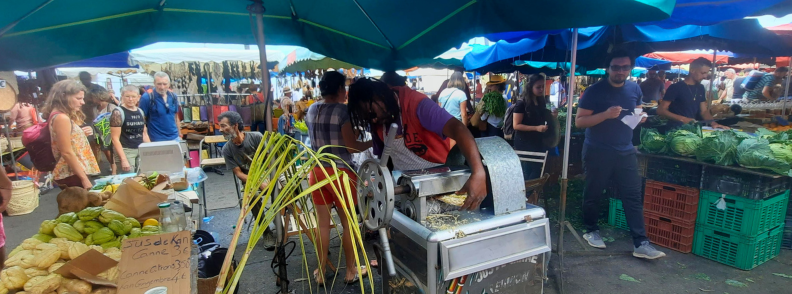 Vendor pressing fresh sugarcane juice at the Saint Paul market on Reunion Island surrounded by local produce stalls and shoppers