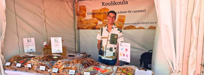 foire de brignoles koulikoula artisanal caramel stand provence fair Koulikoula stand at the Foire de Brignoles displaying artisanal caramels, with the producer smiling behind a table filled with handmade sweets.