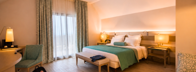 Bright and stylish hotel room at Akoya Hotel & Spa in Saint-Gilles with a king-size bed, modern lighting, and teal decor overlooking a furnished balcony.