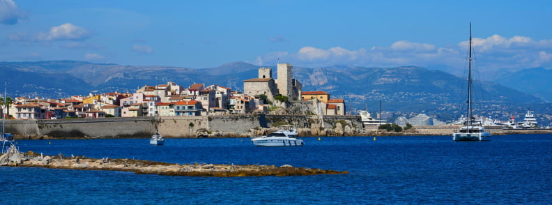 Antibes Old Town After Posidonia Visit Antibes Old Town seen from the sea after a Posidonia Antibes visit, with the old ramparts, Château Grimaldi, boats, and mountains behind the Riviera coast.