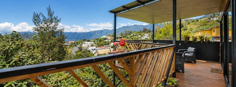 Mountain-view terrace with wooden railings and shaded seating at Gîte Le Panorama in La Réunion.
