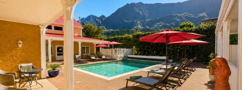 Hotel Le Cilaos with a central pool, red umbrellas, lounge chairs, and dramatic Cirque de Cilaos mountain views in the background.