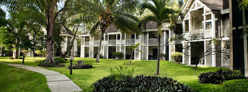 LUX Saint Gilles Resort garden with manicured lawns and colonial-style guesthouse buildings shaded by palm trees.