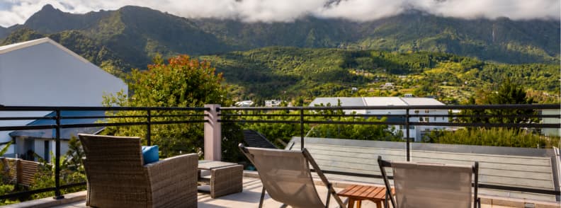 Terrace of La Villa Kazuera in Cilaos with lounge chairs, small table, and panoramic view of the mountains under cloud cover.
