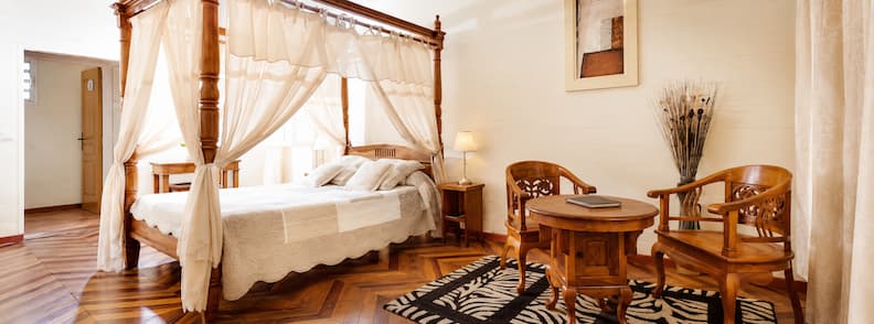 Elegant colonial-style bedroom with canopy bed and wooden furniture at Le Relais des Gouverneurs in Hell-Bourg, Salazie.