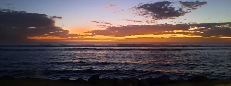 Colorful sunset over the Indian Ocean in Saint-Leu, La Réunion, with dark waves and silhouetted clouds reflecting golden and purple tones.