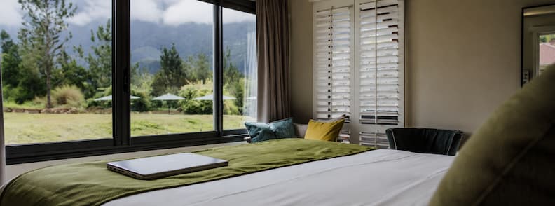Modern hotel room at Sarana Hôtel & Spa with mountain views through large windows and a closed laptop on the bed.