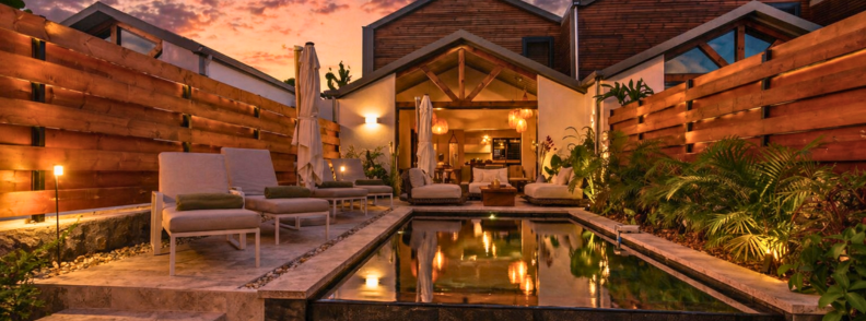 Dusk view of Villa Kintana in Saint-Joseph with a private pool, lounge chairs, and warm ambient lighting reflecting off the water.