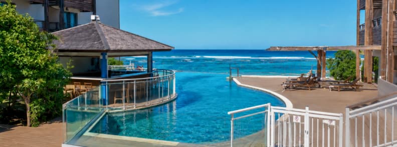 Infinity pool and ocean view from Le Battant des Lames hotel in Saint-Pierre, La Réunion, with deck chairs and wooden structures under clear blue skies.