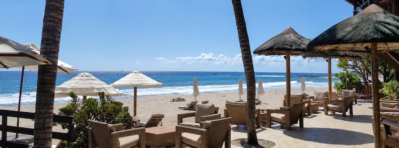 Beachfront lounge area at Le Saint Alexis Hotel & Spa in Saint-Gilles with wicker seating, thatched umbrellas, and a clear view of the lagoon and Indian Ocean.