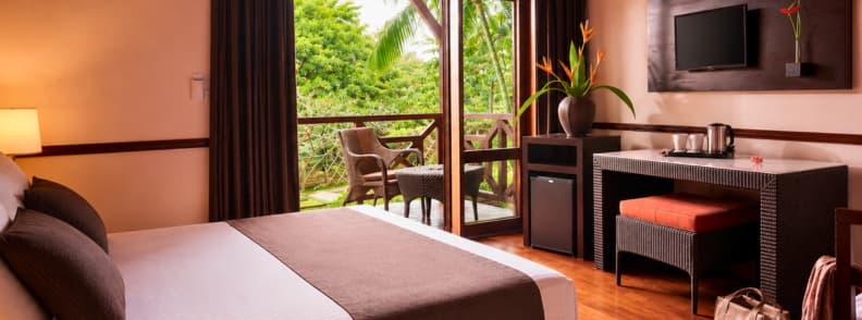 Tropical-style room at Iloha Seaview Hotel in Saint-Leu, featuring a garden-view terrace, warm wooden furnishings, and a cozy desk area with personal touches.