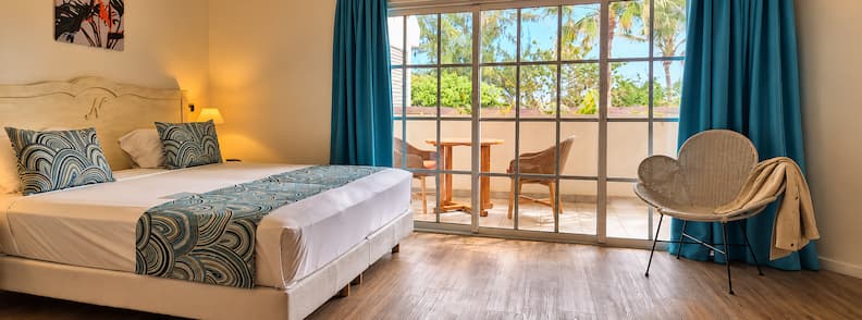 Bright and spacious family-friendly room at Le Nautile Beachfront in La Réunion with double bed, balcony, and view of tropical trees.